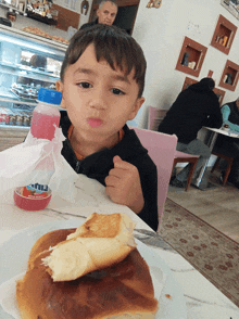 a young boy is sitting at a table with a sandwich and a bottle of aquafina water