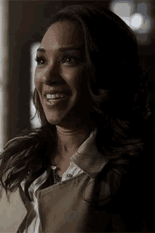 a woman wearing a trench coat and a white shirt is smiling in a dark room .