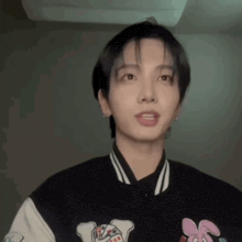 a young man wearing a black and white baseball jacket with a pink bunny on it is looking at the camera .