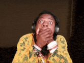 a man wearing headphones and a yellow shirt has a bracelet on his wrist that says i 'm a troll