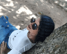 a woman wearing sunglasses rests her head on a tree trunk