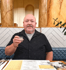 a man sitting at a table holding a shot glass in front of a menu