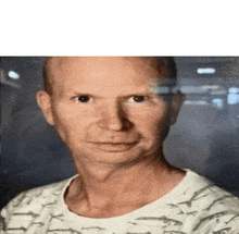 a bald man wearing a white shirt with sharks on it is standing in front of a window and looking at the camera .