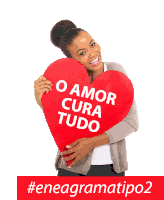 a woman is holding a large red heart that says o amor cura tudo