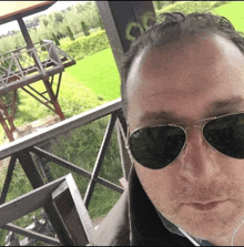 a man wearing ray-ban sunglasses takes a selfie on a balcony