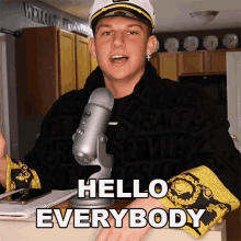 a man in a captain 's hat stands in front of a microphone and says " hello everybody "