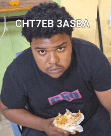 a man wearing a shirt that says cht7eb 3asba eating a sandwich