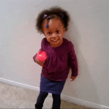 a little girl in a purple shirt is holding a pink ball and smiling