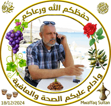 a man sits at a table talking on a cell phone surrounded by grapes and flowers