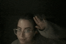 a woman wearing glasses is waving at the camera in the dark