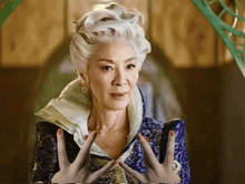 a woman with gray hair is wearing a blue jacket and holding her hands up in the air .
