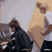 a man wearing a mask is standing next to another man playing a piano ..