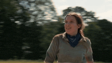a woman wearing a bandana around her neck is smiling in a field