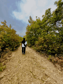 a person walking down a dirt path with trees on the side