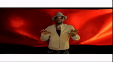 a man wearing a hat and sunglasses is dancing in front of a red background