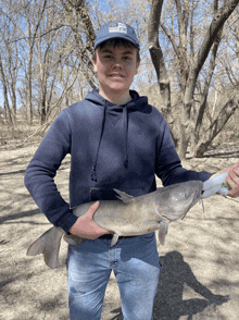 a young man in a blue hat holds a large fish in his hands