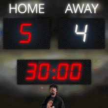 a man stands in front of a scoreboard that says home and away on it