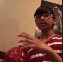 a young boy wearing glasses and a striped shirt is holding a red bottle