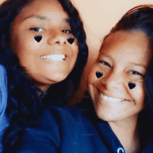 two girls with black hearts on their faces are smiling