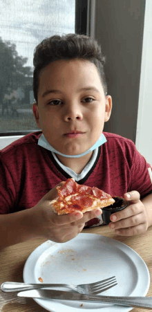 a young boy wearing a mask is eating a pepperoni pizza