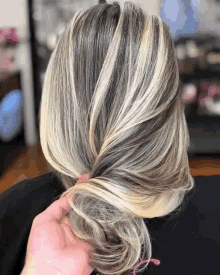 a woman with blonde and gray hair is getting her hair done in a bun .