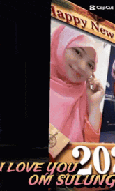 a woman in a pink hijab stands in front of a sign that says i love you om sulung