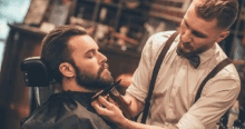 a barber is cutting a man 's beard with a clipper in a barber shop .