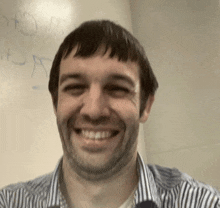 a man in a striped shirt is smiling in front of a whiteboard that says " a " on it