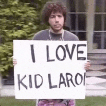 a man with curly hair is holding a sign that says `` i love kid laroi '' .