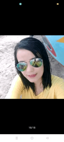 a woman wearing sunglasses and a yellow shirt takes a selfie on the beach .