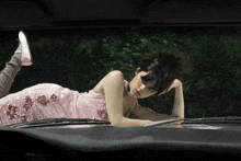 a woman in a pink dress is laying on a car hood