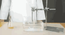 a person in a lab coat is standing in front of a table with a beaker and a container of water .