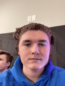 a young man wearing a blue sweatshirt looks at the camera