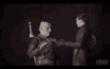 a man in armor is shaking hands with a woman in a dark room with hbo written on the bottom right