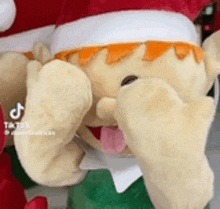 a stuffed animal with a tongue sticking out is wearing a santa hat and a green shirt .