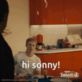 a man sitting at a table says hi sonny in a kitchen