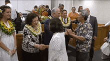 a group of people shaking hands with one wearing a lei of flowers