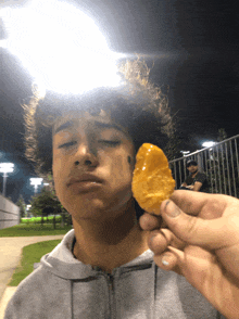 a young man with curly hair is holding a fried potato chip in front of his face