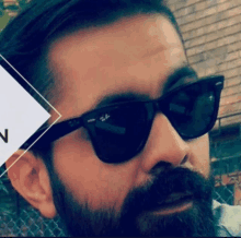 a man with a beard wearing ray-ban sunglasses looks at the camera