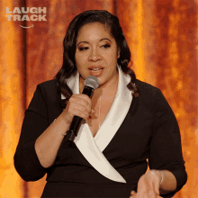 a woman in a black and white dress holds a microphone in front of a sign that says laugh track