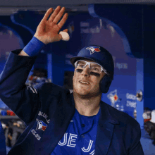 a man wearing a blue jays jacket and helmet waves his hand