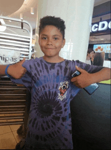 a young boy wearing a purple tie dye shirt is giving a thumbs up sign