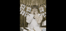 a young man is sitting at a table in front of a gold curtain with a happy birthday banner .