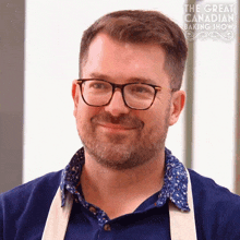 a man wearing glasses and a blue shirt is smiling in front of a sign that says the great canadian baking show