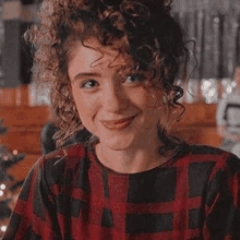 a woman with curly hair is wearing a plaid shirt and smiling .