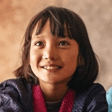 a young girl is smiling for the camera and wearing a pink scarf .