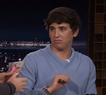 a young man in a blue sweater is giving a thumbs up sign
