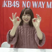 a woman giving the ok sign in front of a sign that says " akb48 no way m "