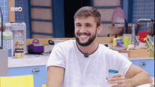 a man with a beard is smiling while holding a glass in front of a bbbo sign