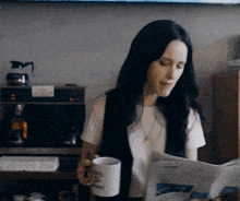 a woman is reading a newspaper while holding a mug